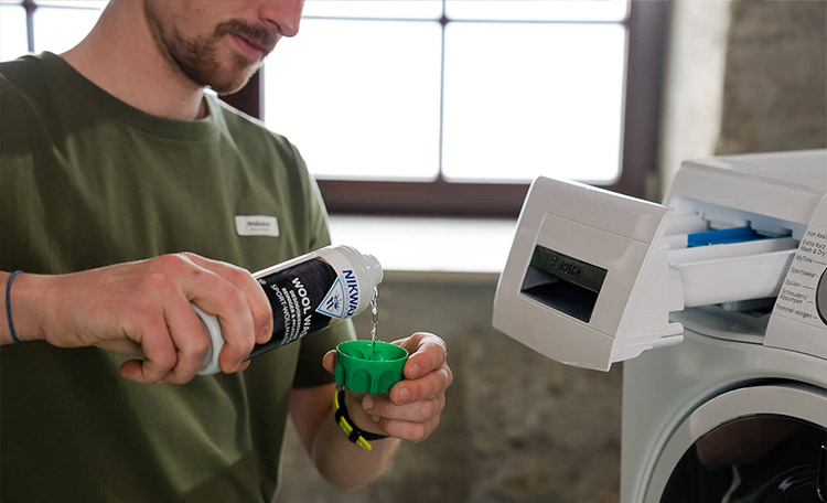 Man doet wolwasmiddel in de wasmachine
