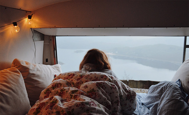 Eine Frau nestelt sich in een warme deken in een camper en kijkt uit het raam.