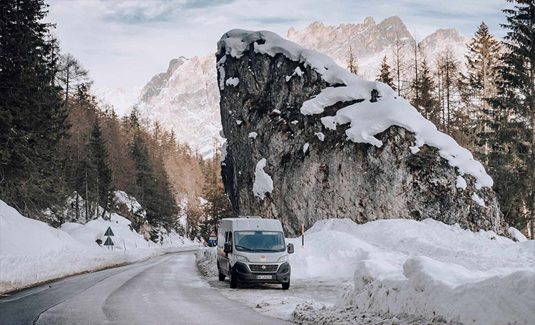 Het rijden in de winter vereist voorzichtigheid en oefening – vooral met een grote camper. Camper op een besneeuwde weg in de bergen.